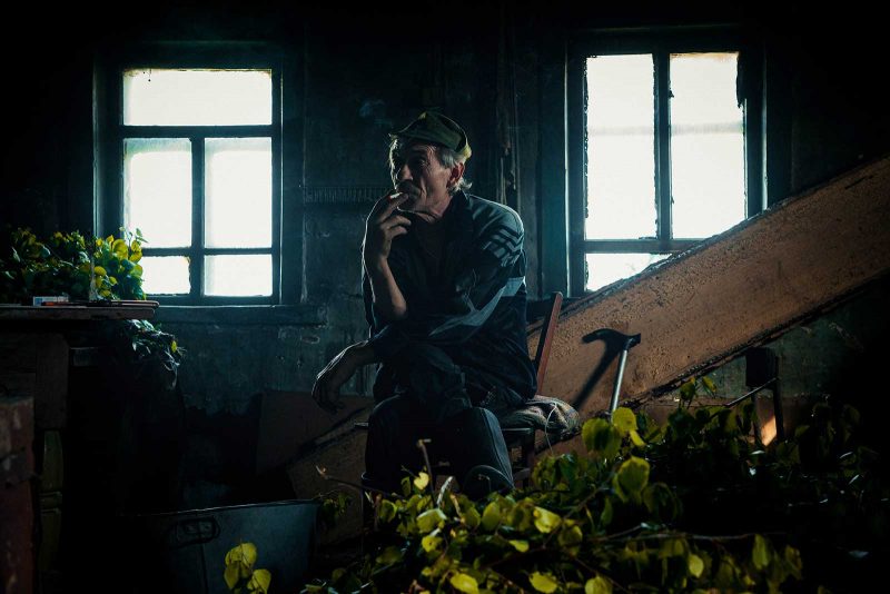 Old man sitting in a dark room, staring, smoking a cigarette
